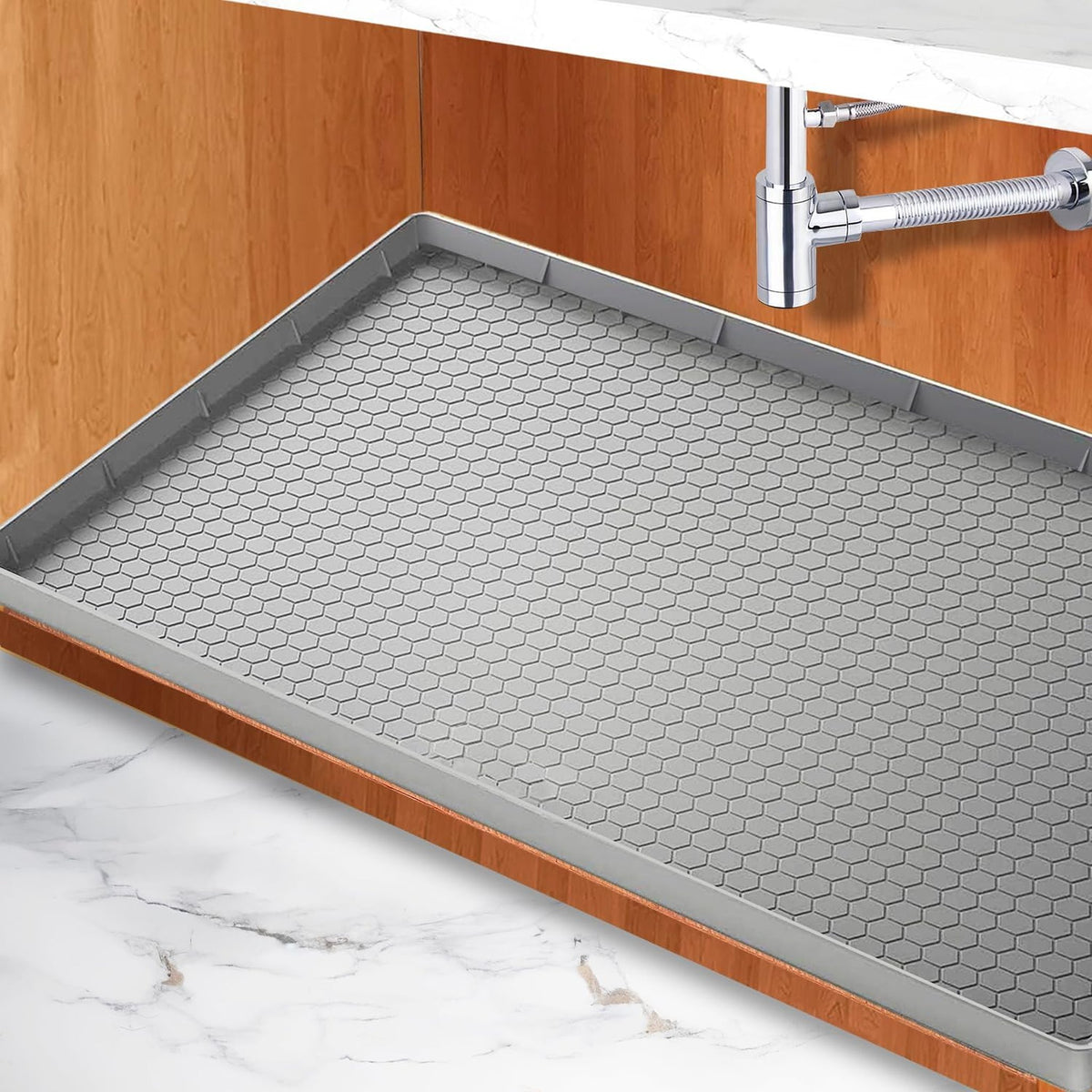 Under-sink leak mat: gray silicone mat lining the floor of a kitchen sink cabinet below the drain pipe.